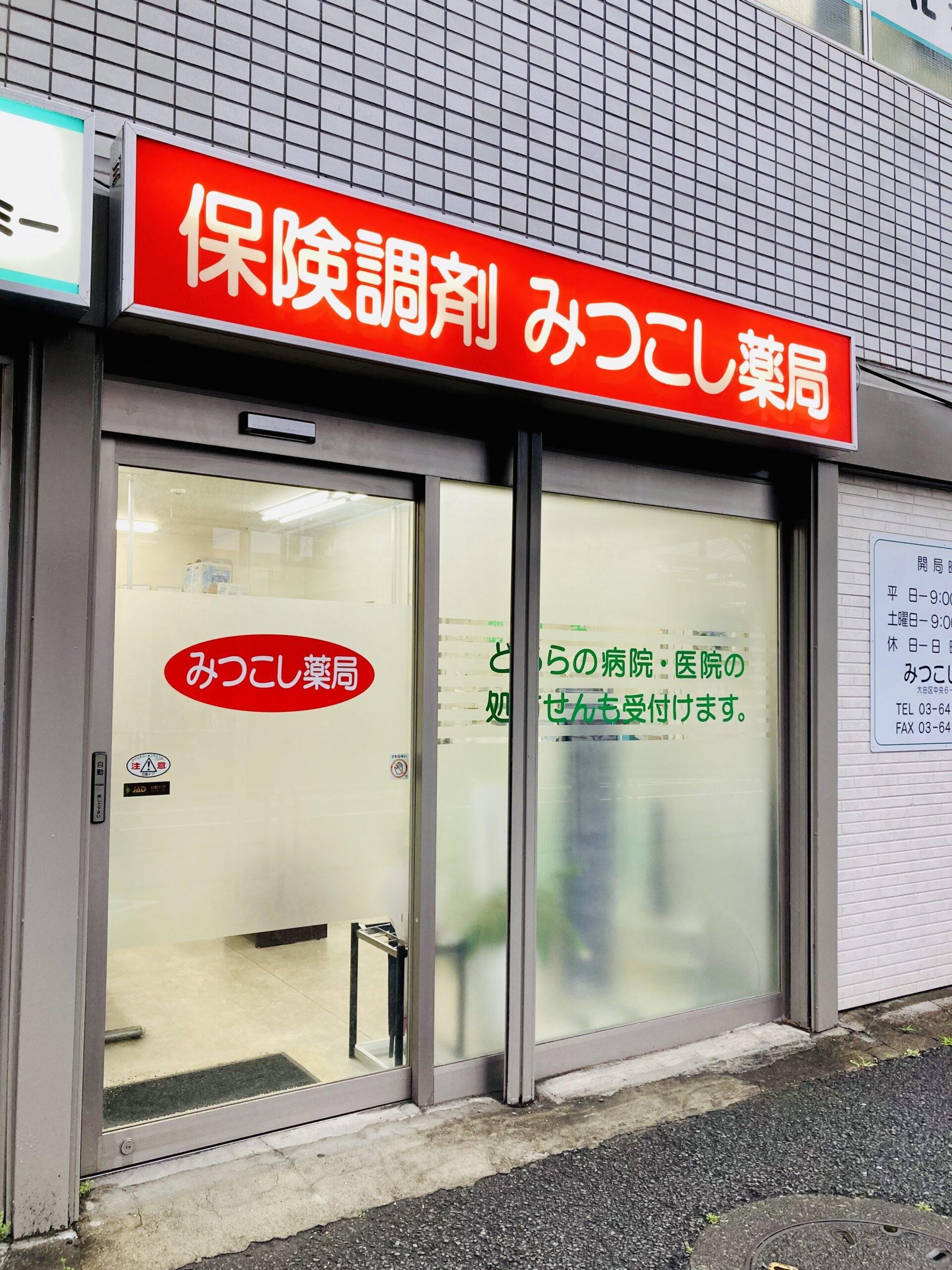 赤い「みつこし薬局」の看板とガラス扉の入口